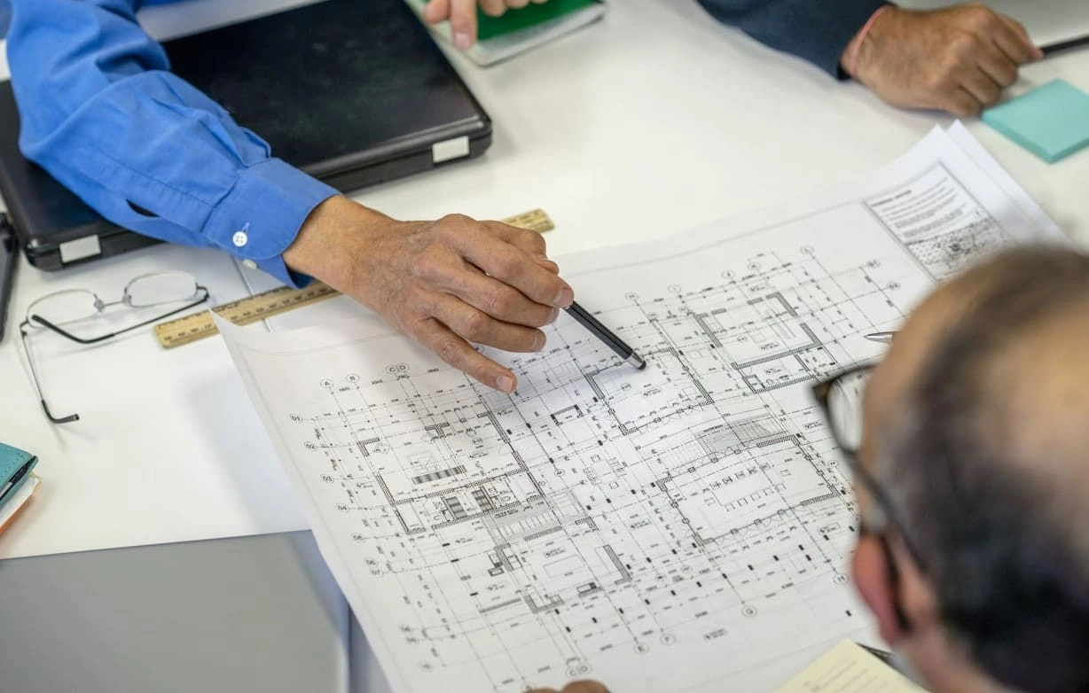 Coworkers discussing a blueprint generated in-house with a new blueprint printing machine Coworkers discussing a blueprint generated in-house with a new blueprint printing machine